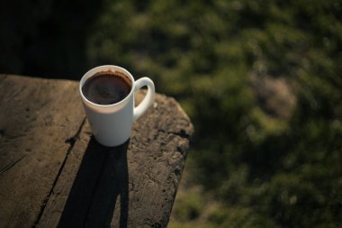 Bahçedeki ahşap bir masada bir fincan kahve duruyor.