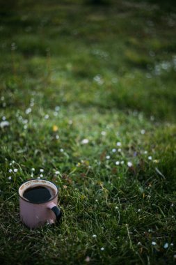 Güneşli bir günde, içinde kahve ve çay olan metal bir bardak ahşap bir platformda oturuyor..