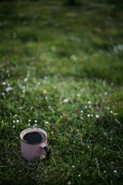 Güneşli bir günde, içinde kahve ve çay olan metal bir bardak ahşap bir platformda oturuyor..