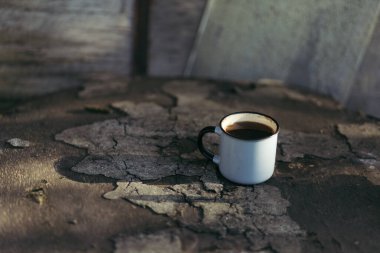 Güneşli bir günde, içinde kahve ve çay olan metal bir bardak ahşap bir platformda oturuyor..