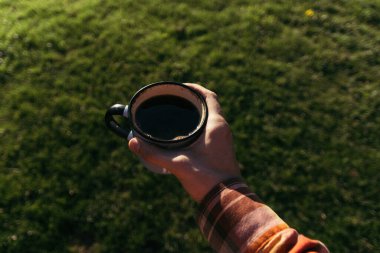 Güneşli bir günde, içinde kahve ve çay olan metal bir bardak ahşap bir platformda oturuyor..