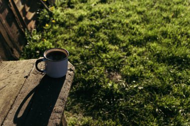 Güneşli bir günde, içinde kahve ve çay olan metal bir bardak ahşap bir platformda oturuyor..