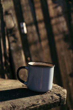 Güneşli bir günde, içinde kahve ve çay olan metal bir bardak ahşap bir platformda oturuyor..