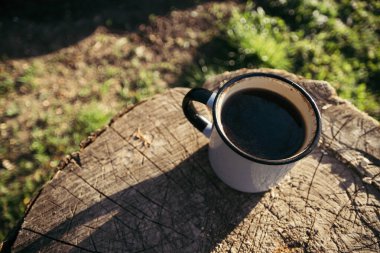 Güneşli bir günde, içinde kahve ve çay olan metal bir bardak ahşap bir platformda oturuyor..