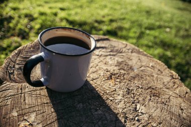 Güneşli bir günde, içinde kahve ve çay olan metal bir bardak ahşap bir platformda oturuyor..