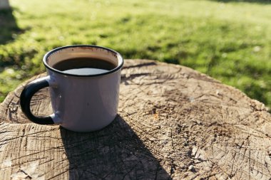 Güneşli bir günde, içinde kahve ve çay olan metal bir bardak ahşap bir platformda oturuyor..
