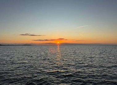 Fehmarn, Almanya 'da, sakin Baltık Denizi üzerinde gün batımı. Bulutların arkasından parlayan güneş ve suyun üzerindeki parlak yansıma. Seçici odak