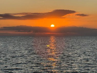 Fehmarn, Almanya 'da, sakin Baltık Denizi üzerinde gün batımı. Bulutların arkasından parlayan güneş ve suyun üzerindeki parlak yansıma. Seçici odak