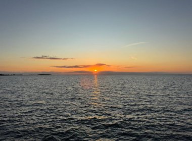 Fehmarn, Almanya 'da, sakin Baltık Denizi üzerinde gün batımı. Bulutların arkasından parlayan güneş ve suyun üzerindeki parlak yansıma. Seçici odak