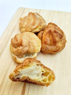 Yakın planda, açık tahta bir tahtaya yerleştirilmiş, klasik bir tatlı olarak sevilmeye hazır bir kaç mükemmel altın-kahverengi kremalı puf sergileniyor..