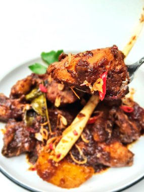 Endonezya tavuk yemeğinin yakın plan bir resmi, zengin, koyu soya sosunda pişirilmiş, aromatik otlar ve baharatlarla servis ediliyor..