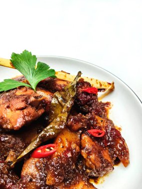 Endonezya tavuk yemeğinin yakın plan bir resmi, zengin, koyu soya sosunda pişirilmiş, aromatik otlar ve baharatlarla servis ediliyor..