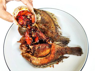 İki kızartılmış tilapia balığının yakın çekimi beyaz bir tabakta, yanında baharatlı biber sambal, popüler ve lezzetli bir Asya yemeği..