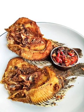 İki kızartılmış tilapia balığının yakın çekimi beyaz bir tabakta, yanında baharatlı biber sambal, popüler ve lezzetli bir Asya yemeği..
