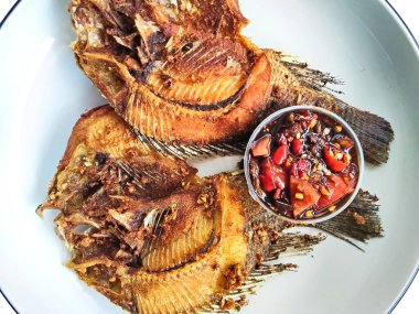 İki kızartılmış tilapia balığının yakın çekimi beyaz bir tabakta, yanında baharatlı biber sambal, popüler ve lezzetli bir Asya yemeği..