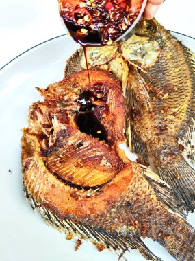 İki kızartılmış tilapia balığının yakın çekimi beyaz bir tabakta, yanında baharatlı biber sambal, popüler ve lezzetli bir Asya yemeği..