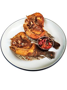 İki kızartılmış tilapia balığının yakın çekimi beyaz bir tabakta, yanında baharatlı biber sambal, popüler ve lezzetli bir Asya yemeği..