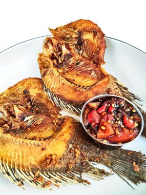 İki kızartılmış tilapia balığının yakın çekimi beyaz bir tabakta, yanında baharatlı biber sambal, popüler ve lezzetli bir Asya yemeği..