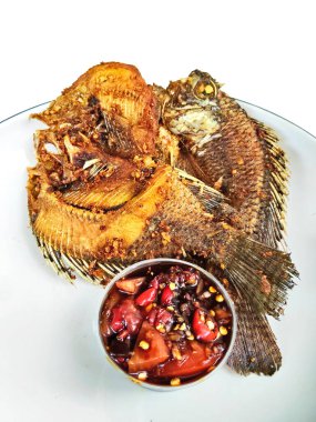 İki kızartılmış tilapia balığının yakın çekimi beyaz bir tabakta, yanında baharatlı biber sambal, popüler ve lezzetli bir Asya yemeği..