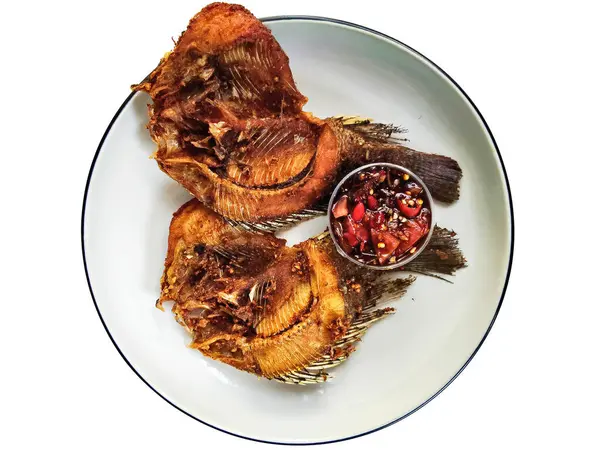 İki kızartılmış tilapia balığının yakın çekimi beyaz bir tabakta, yanında baharatlı biber sambal, popüler ve lezzetli bir Asya yemeği..