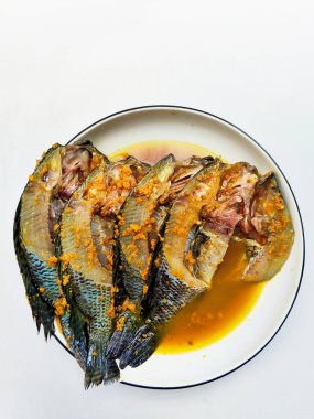 Bir tabak çiğ, taze tilapia balığı aromalı, geleneksel baharat salamurasıyla kaplanmış, pişirmeye hazır..