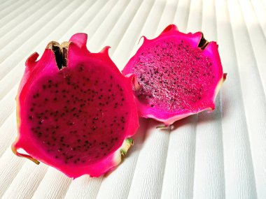 Yeni kesilmiş bir ejderha meyvesinin yakın çekimi canlı mor et ve siyah tohumlarını dokulu beyaz bir arka planda ortaya çıkarıyor..