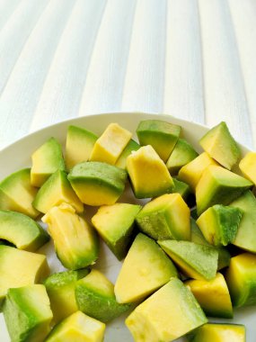 Taze doğranmış yeşil ve sarı avokado parçaları beyaz bir kasede, sağlıklı yağları, canlı renkleri ve mutfak projelerinde temiz beslenmeyi vurgulamak için mükemmel..