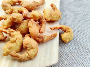 Hafif bir ahşap kesme tahtasının üzerine yumuşak odaklı bir kabarık çuval bezi arka planına karşı bir yığın altın kahverengi çıtır karides (Ebi Fry veya Tempura) yerleştirilir..