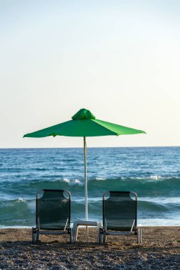 Plaj şezlongları yeşil şemsiyelerin altında deniz kenarında, tatil ve rahatlama konsepti, gün doğumu, yaz güneşli günü, mavi gökyüzü fotokopi alanı