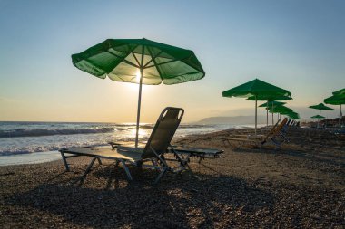 Plaj şezlongları yeşil şemsiyelerin altında deniz kenarında, tatil ve rahatlama konsepti, gün doğumu, yaz güneşli günü, mavi gökyüzü fotokopi alanı