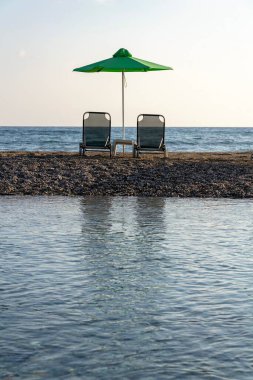 Plaj şezlongları şemsiyelerin altında kumlu yarımadada Georgioupoli, Girit yakınlarında deniz ve nehir arasında, güneşli yaz günü şafak vakti, rahatlama konsepti, açık mavi gökyüzü boşluğu