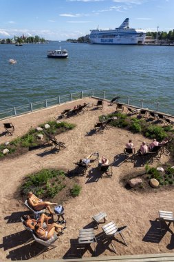 HELSINKI, FINLAND - 6 Temmuz 2024: Halk deniz yüzme havuzu ve geleneksel saunanın keyfini çıkaran insanlar güneşli bir yaz gününde 6 Temmuz 2024 'te Finlandiya' nın Helsinki kentinde Katadanokanlaituri 'de.