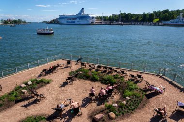 HELSINKI, FINLAND - 6 Temmuz 2024: Halk deniz yüzme havuzu ve geleneksel saunanın keyfini çıkaran insanlar güneşli bir yaz gününde 6 Temmuz 2024 'te Finlandiya' nın Helsinki kentinde Katadanokanlaituri 'de.