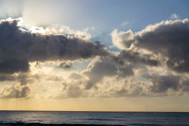 Breathtaking sunrise with sun hiding behind cloud, sea waves and blue sky with copy space clipart