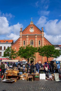 İnsanlar 26 Mayıs 2026 'da Brüksel, Belçika' da, Place du Jeu de Balle 'de, arka planda bulunan Meryem Ana Kilisesi' nde bitpazarından eski antika şeyler satın alıyorlar..