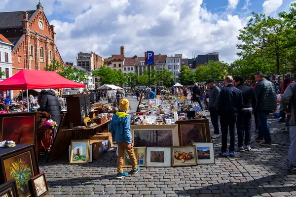 İnsanlar 26 Mayıs 2026 'da Brüksel, Belçika' da, Place du Jeu de Balle 'de, arka planda bulunan Meryem Ana Kilisesi' nde bitpazarından eski antika şeyler satın alıyorlar..