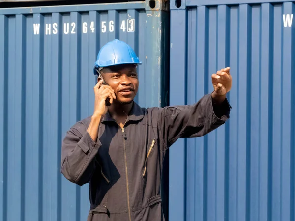Foreman engineer black skin african person people blue hardhat helmet safety engineer professional industry manager supervisor pointing finger talk discuss mobile telephone import export  container