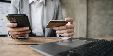 Mutlu Asyalı İş kadını ofisteki cep telefonunu kullanarak internetten ödeme yapıyor.