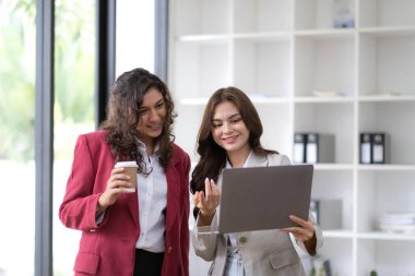 Two beautiful Asian businesswomen standing using digital tablet consulting and analyzing information in office work...