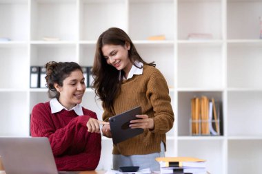 Two young Asian business woman talk, consult, discuss working with new startup project idea presentation analyze plan marketing and investment in the office...