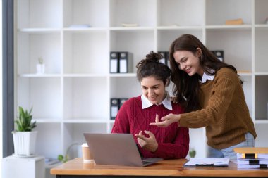 Two young Asian business woman talk, consult, discuss working with new startup project idea presentation analyze plan marketing and investment in the office...