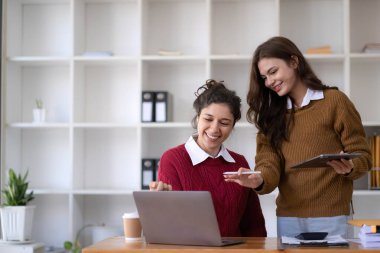 Two young Asian business woman talk, consult, discuss working with new startup project idea presentation analyze plan marketing and investment in the office...
