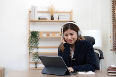 Gülümseyen kız evde dinleniyor dizüstü bilgisayarıyla müzik dinliyor ve beyaz kulaklık takıyor.