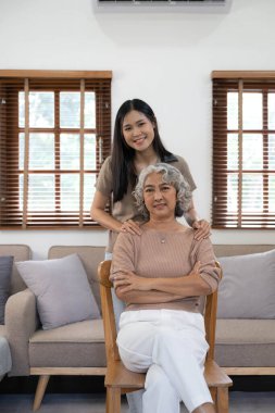 Asyalı sevimli bir ailenin portresi, genç bir kızın yaşlı bir anneye sarılması. Çekici bir kadın ve yaşlı olgun bir anne kanepede oturup birlikte oturma odasında eğleniyorlar..