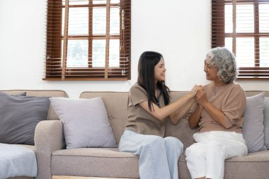 Asyalı sevimli bir ailenin portresi, genç bir kızın yaşlı bir anneye sarılması. Çekici bir kadın ve yaşlı olgun bir anne kanepede oturup birlikte oturma odasında eğleniyorlar.