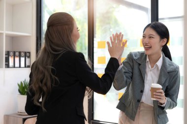 Genç Asyalı iş adamları yaratıcı iş adamları ofiste başarılı iş arkadaşları başarıyı ve başarı kavramını kutlayan ortaklık çalışmalarından mutluluk duyarlar.