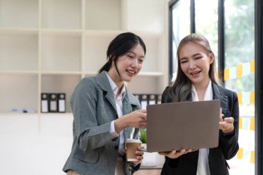 Two beautiful Asian businesswomen standing using digital tablet consulting and analyzing information in office work...