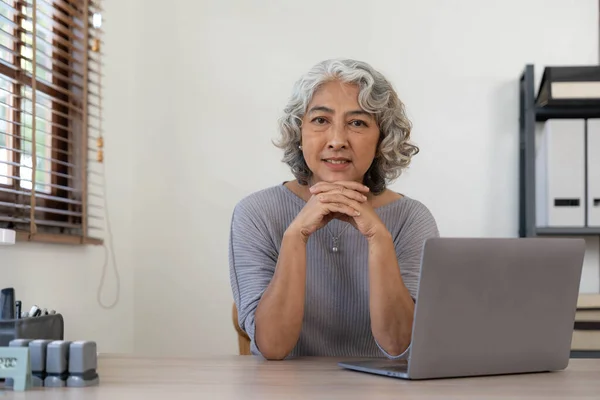 Portrait of smiling asian senior mature middle aged businesswoman using laptop working and web surfing on desk