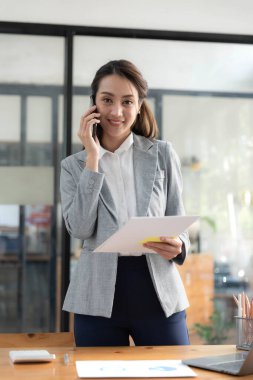 İş yerinde elinde cep telefonu tutan takım elbiseli mutlu Asyalı iş kadını duruyor.. 