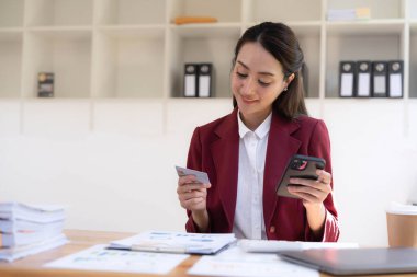 Mutlu Asyalı İş kadını ofisteki cep telefonunu kullanarak internetten ödeme yapıyor.